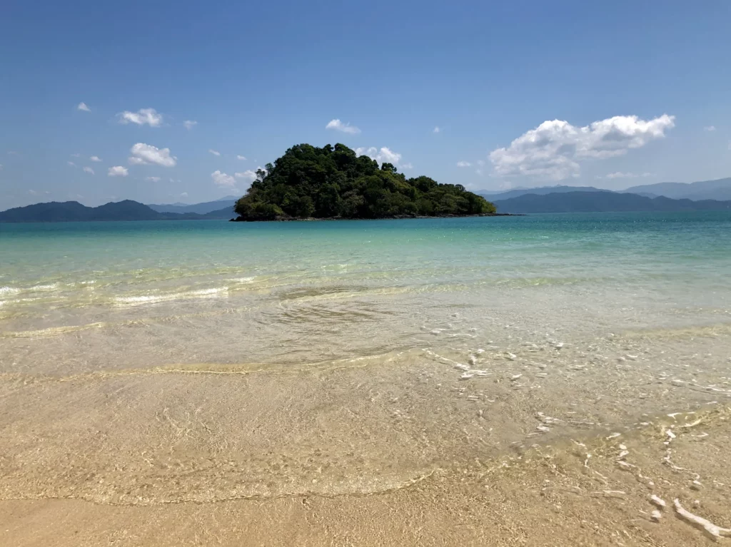 Klares Wasser und bewaldete Kleininsel vor Koh Phayam mit Ranongs Bergen – Foto: Tintin Thaï